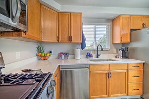Una cocina con armarios de madera, lavavajillas de acero inoxidable, estufa y una ventana con persianas.