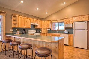 A kitchen with wooden cabinets, a central island with stools, a microwave, a refrigerator, and a dishwasher.