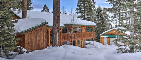 A wooden cabin with a balcony, surrounded by snow-covered trees and a clear sky.