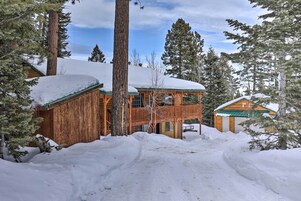 A wooden cabin with a balcony, surrounded by snow-covered trees and a clear sky.