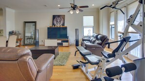 A spacious living room with a large flat-screen TV, leather sofas, a ceiling fan, and a home gym with exercise equipment. - Pet-friendly Houston Home ~ 7 Mi to Downtown! (Houston)