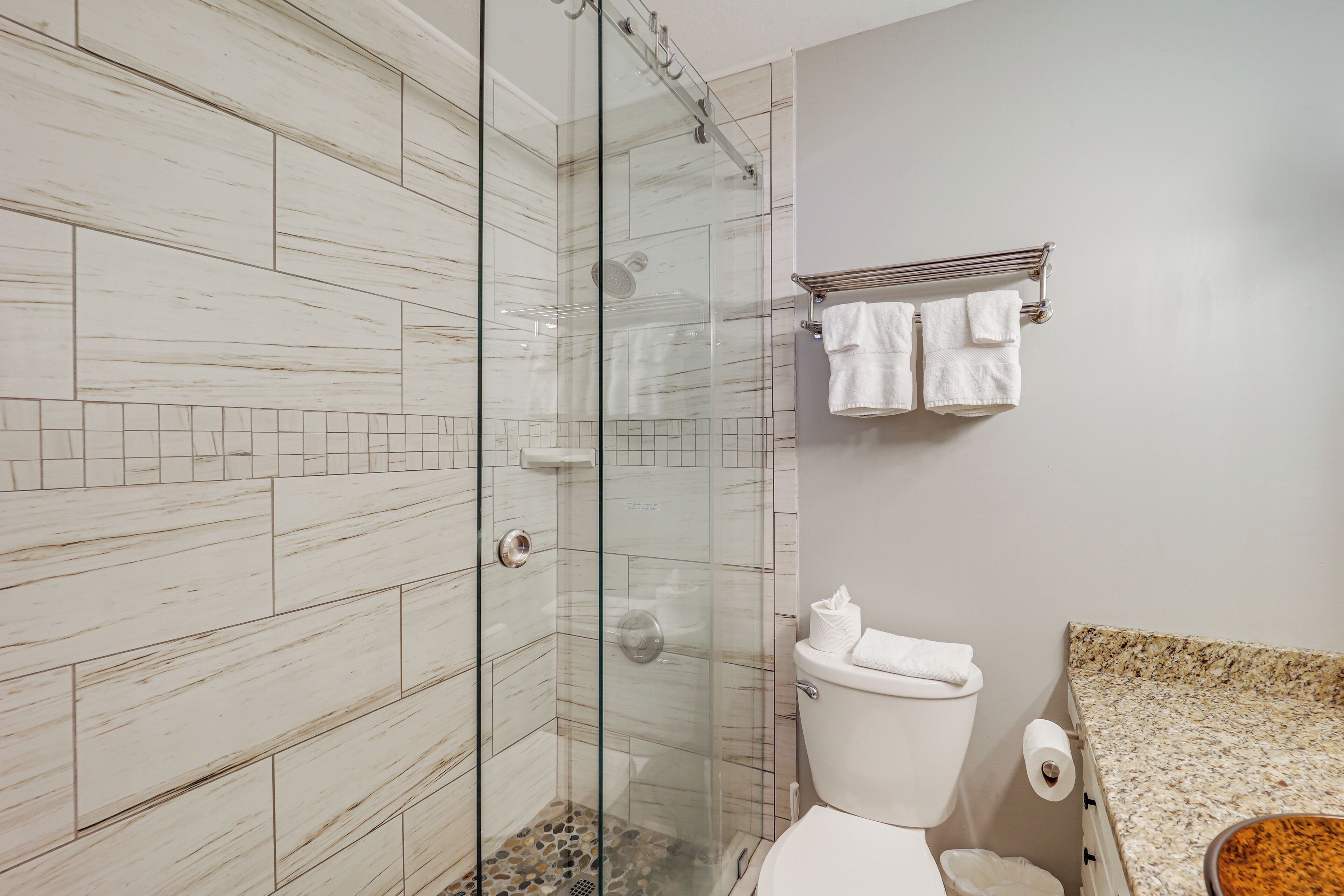 Une salle de bain avec une douche à parois de verre, des toilettes et un comptoir en granit.