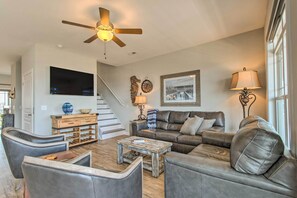 A living room with a ceiling fan, a flat-screen TV, a coffee table, a sofa, and a lamp. - Surf City Escape w/ 6 Decks: Steps To Beach (Holly Ridge)