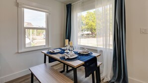 Un coin repas avec une table dressée pour deux personnes, un banc et une vue sur l’extérieur grâce à de grandes fenêtres.