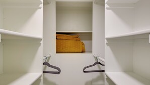 Un placard blanc avec deux tringles pour suspendre les vêtements et une étagère où sont pliées des serviettes jaunes.