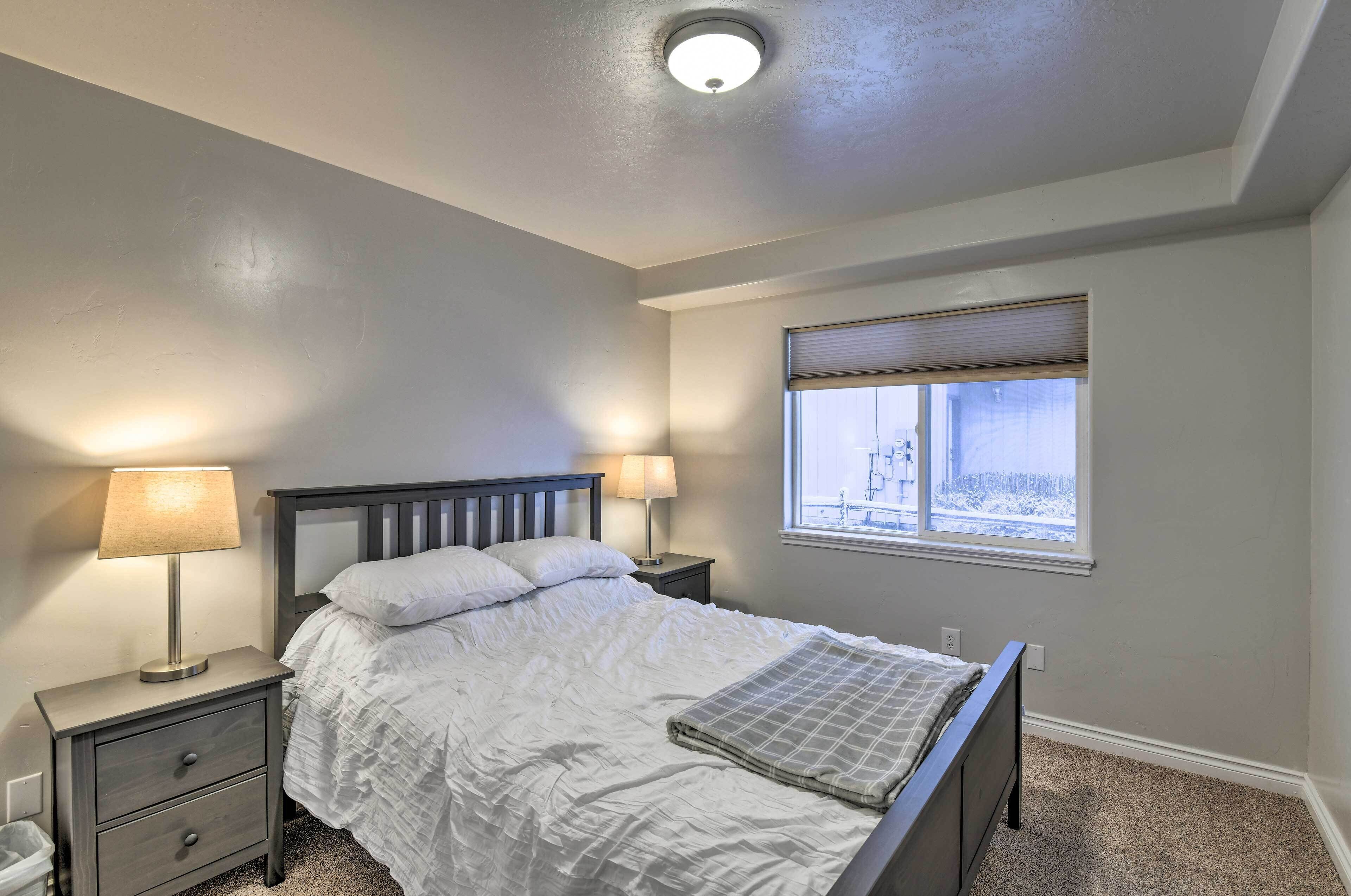 A bedroom with a bed, two bedside tables with lamps, a window with blinds, and a ceiling light.