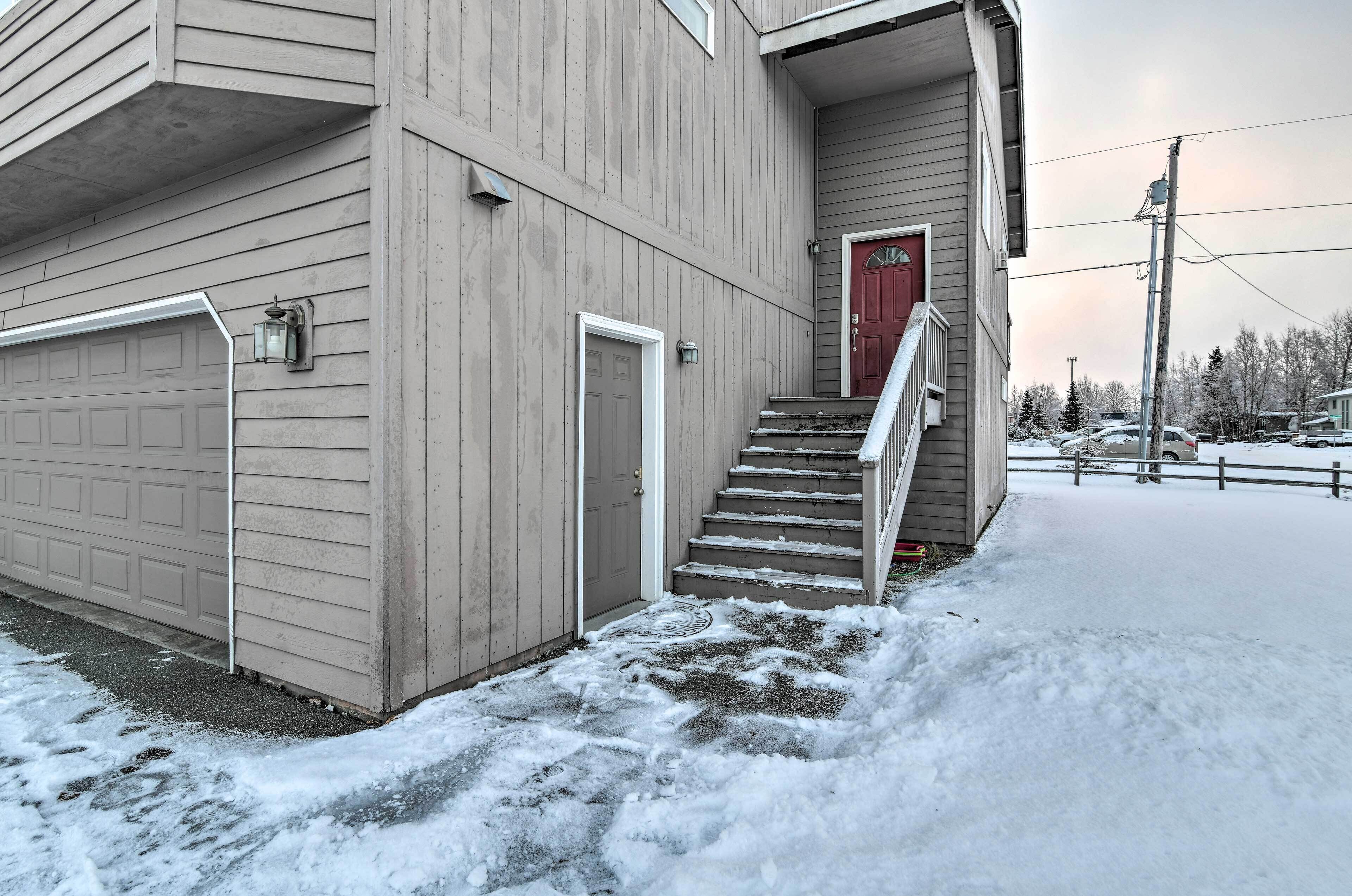 A two-story building with a red door, a garage, and a staircase leading to the second floor.