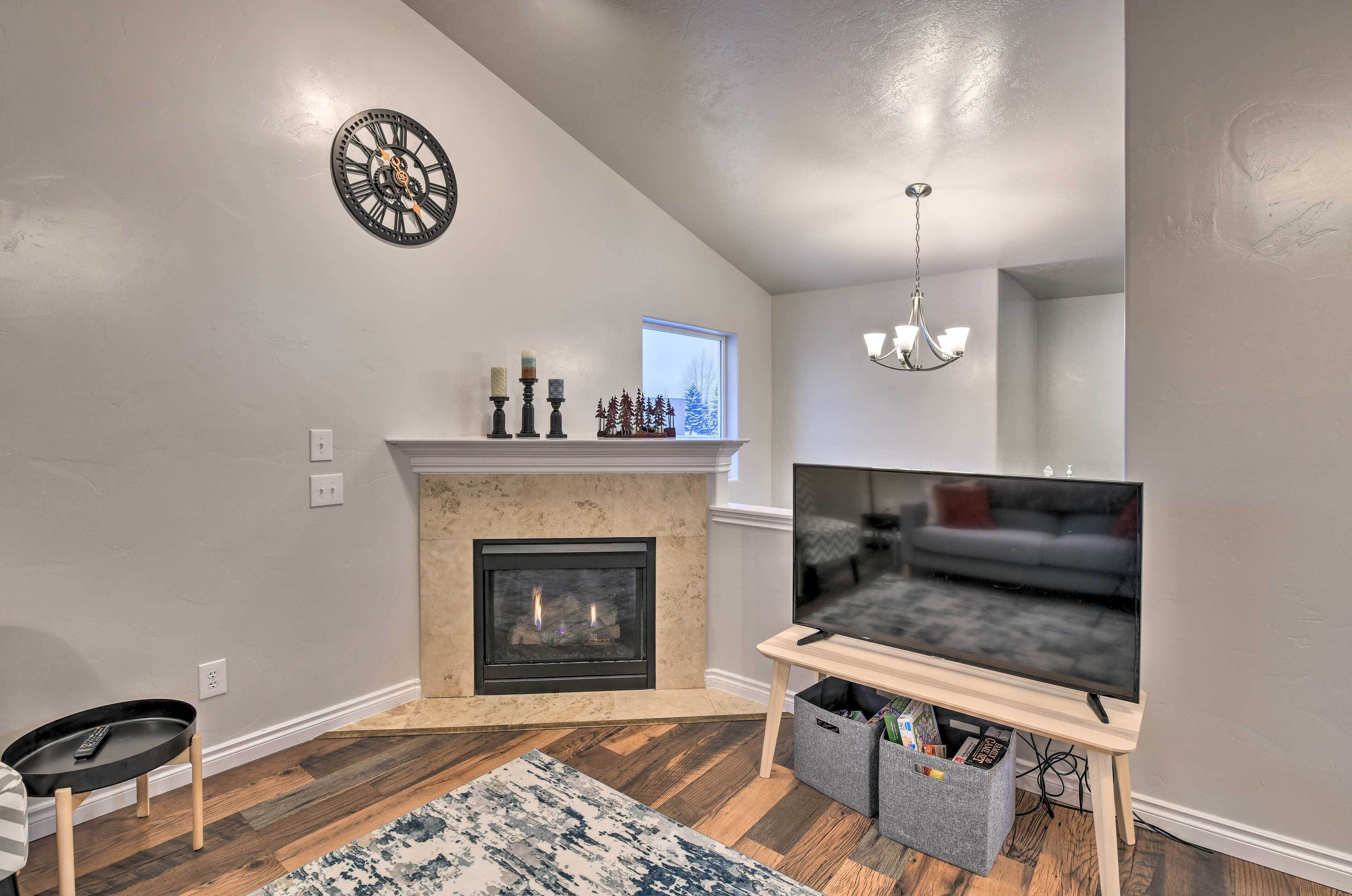 A living room with a fireplace, a television on a stand, a clock on the wall, and a small table with a remote.
