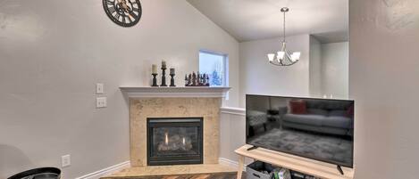 A living room with a fireplace, a television on a stand, a clock on the wall, and a small table with a remote.
