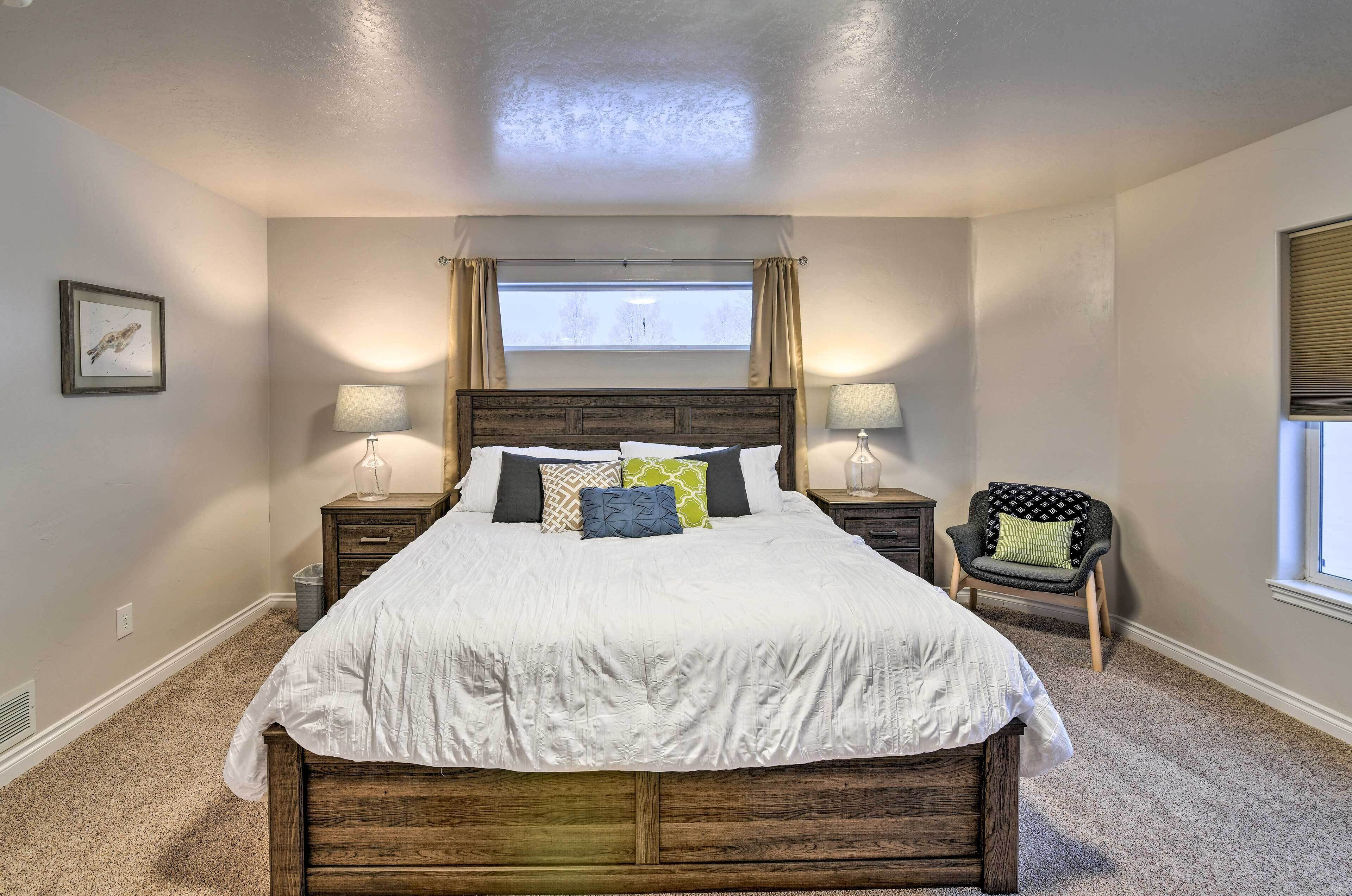 A bedroom with a large bed, two bedside tables with lamps, a chair, and a window with curtains.