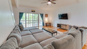 Un salon moderne avec un grand canapé d’angle, une table basse, un téléviseur et un ventilateur de plafond.