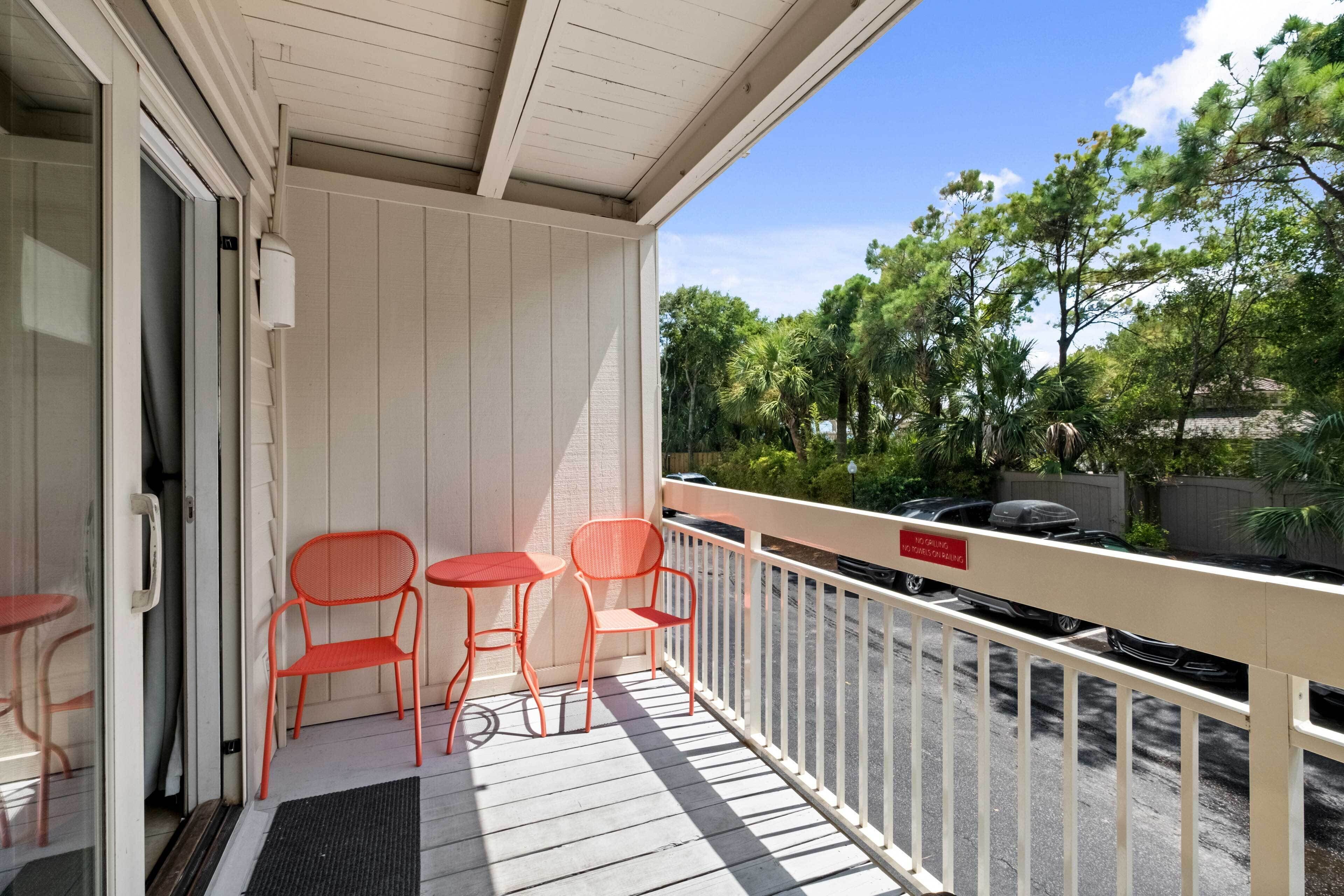 Ein Balkon mit weißer Brüstung, einer Tür und drei orangefarbenen Stühlen.