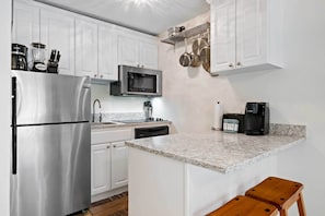 A modern kitchen with white cabinets, stainless steel appliances, a granite countertop, and a wooden stool. - Walk to Bars & Shops: Resort Condo in Hilton Head! (Hilton Head Island)