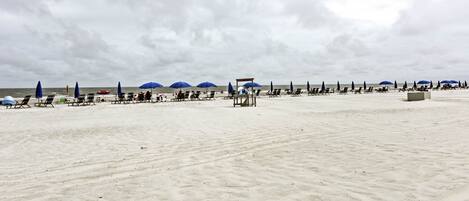 A beach with rows of sun loungers and umbrellas, a lifeguard tower, and the ocean in the background.