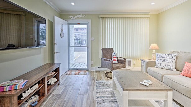 A living room with a sofa, coffee table, and a wicker chair. There is a bench with a 'Welcome' sign and a small table with a lamp. A door leads to an outdoor area. - Brigantine Beach Retreat: Swim, Fish, & Shop! (Brigantine)