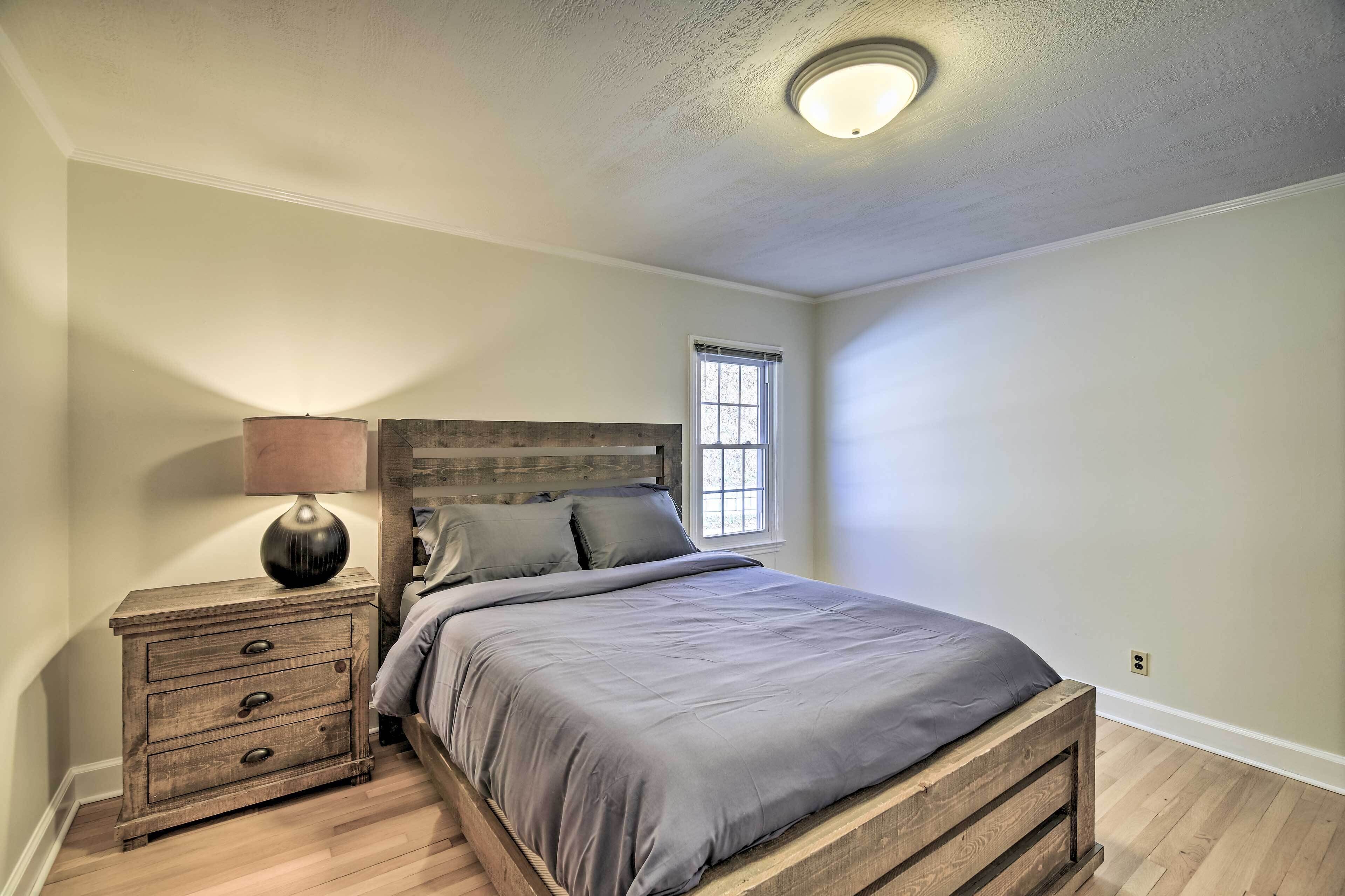 A bedroom with a bed, a nightstand with drawers, a lamp, and a window.