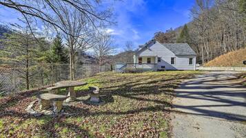 A white house with a stone bench and a picnic table in a wooded area.