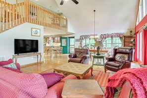 A spacious living room with a wooden staircase, a television, leather armchairs, and a dining area.