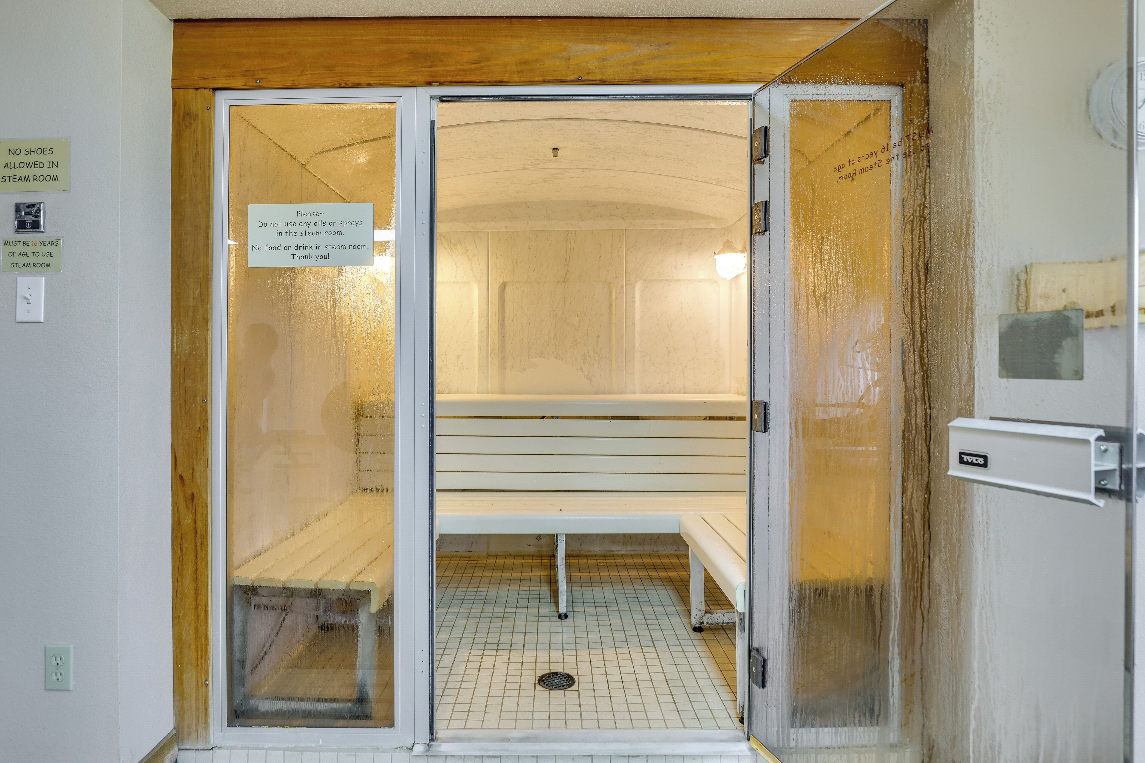 A steam room with a bench, a sign prohibiting food and drink, and a sign indicating no shoes allowed.