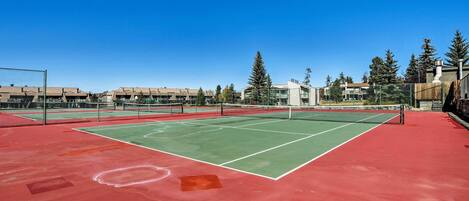 A tennis court with a net, surrounded by buildings and trees.