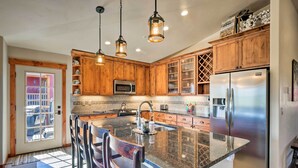 A kitchen with wooden cabinets, a stainless steel refrigerator, and a large island with bar stools. - Winter Park Retreat: Mtn Views & Pool Access! (Fraser)