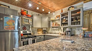 Een moderne keuken met granieten aanrechtbladen, roestvrijstalen apparatuur en houten accenten aan het plafond.