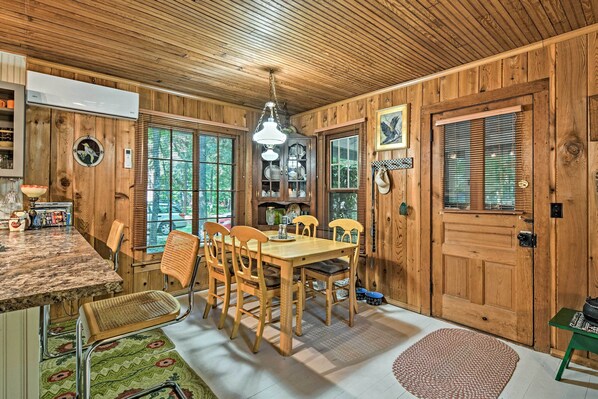 A wooden interior with a dining table, chairs, and a kitchen area with cabinets and a hanging light fixture.
