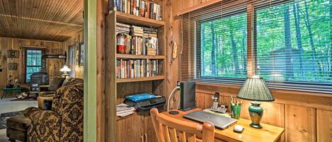 A cozy cabin interior with a wooden desk, bookshelves, and a fireplace.