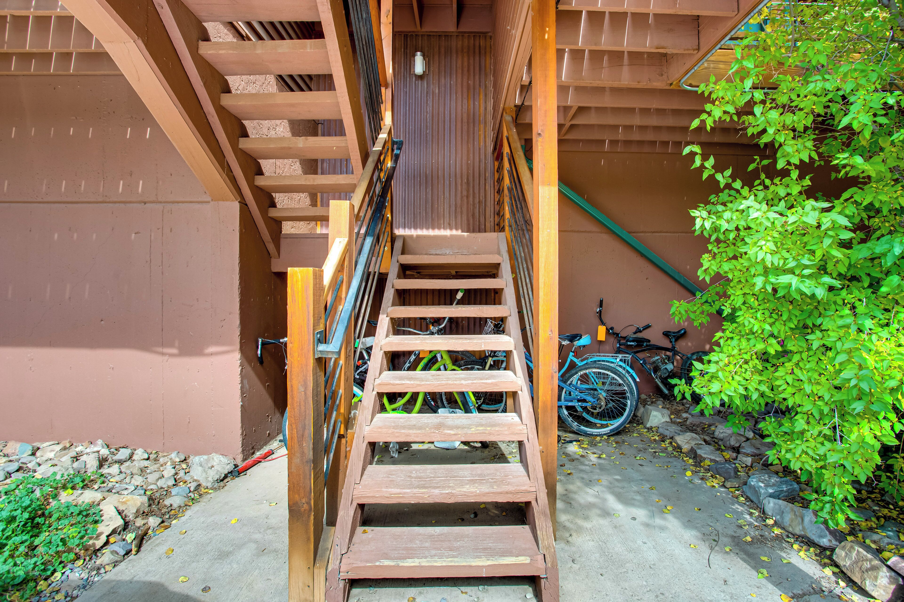 A wooden staircase leading to a building entrance, with bicycles parked nearby and a green bush to the right.