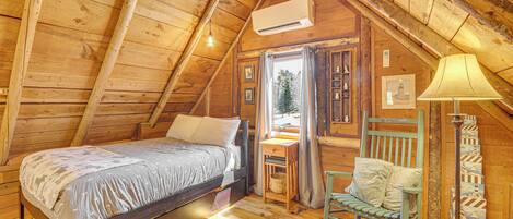 Un dormitorio de cabaña de madera con una cama, un sillón mecedor, una lámpara y una ventana.
