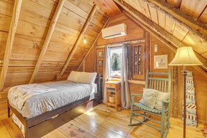 Ein Schlafzimmer einer Holzhütte mit einem Bett, einem Schaukelstuhl, einer Lampe und einem Fenster.