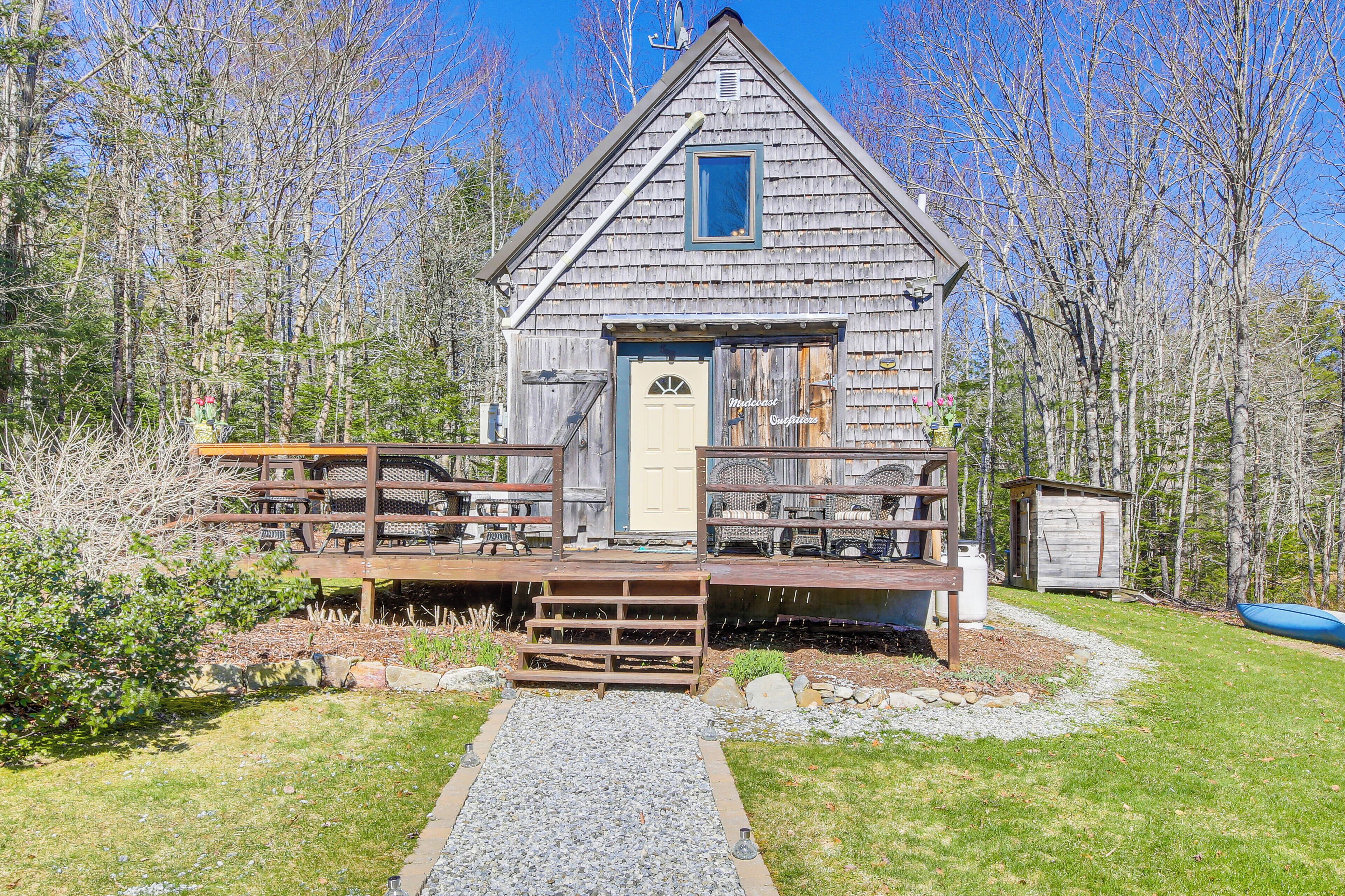 A rustic wooden cabin with a porch, a small shed, and a gravel path leading to the entrance.