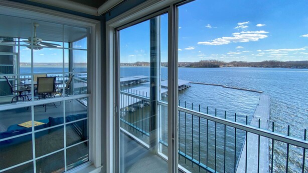 Une pièce dotée de grandes fenêtres donnant sur un plan d’eau, d’un balcon avec une balustrade et d’un ventilateur de plafond.