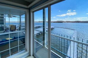Ein Zimmer mit großen Fenstern mit Blick auf ein Gewässer, ein Balkon mit Geländer und ein Deckenventilator.