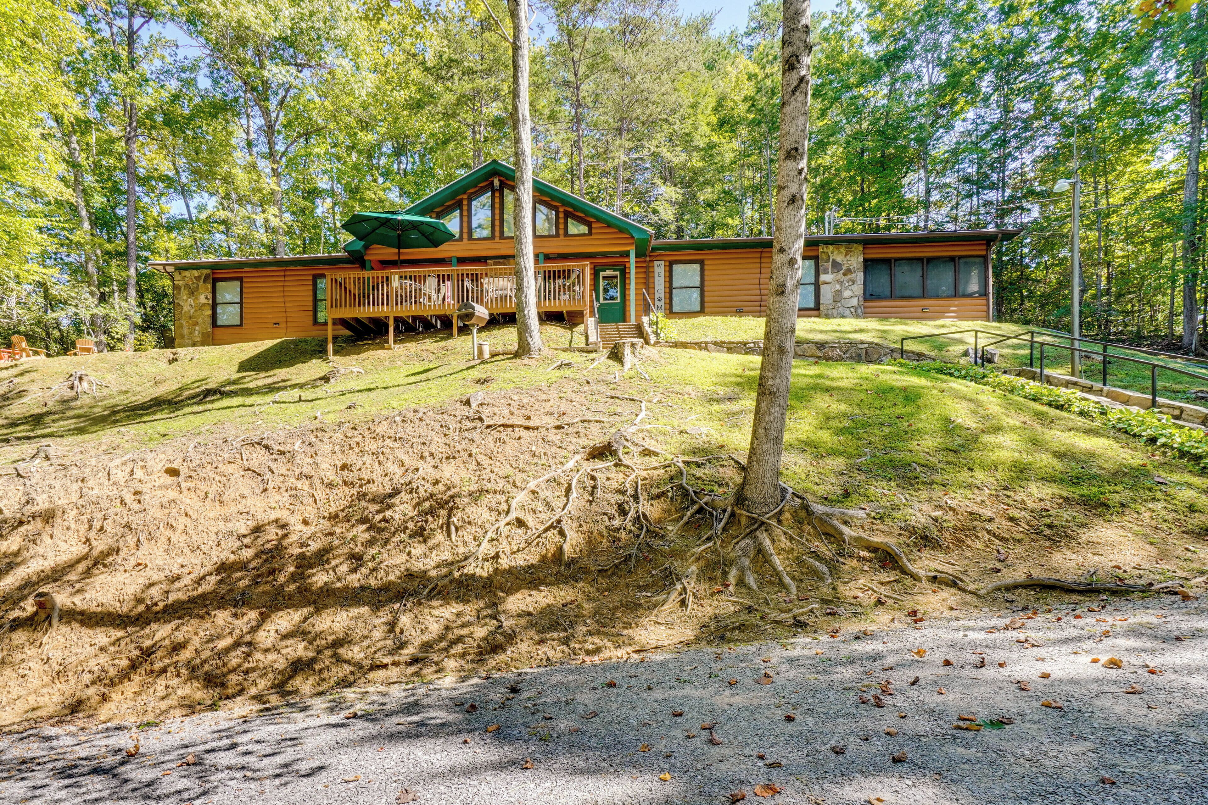 A cabin with a deck, surrounded by trees and a grassy area.