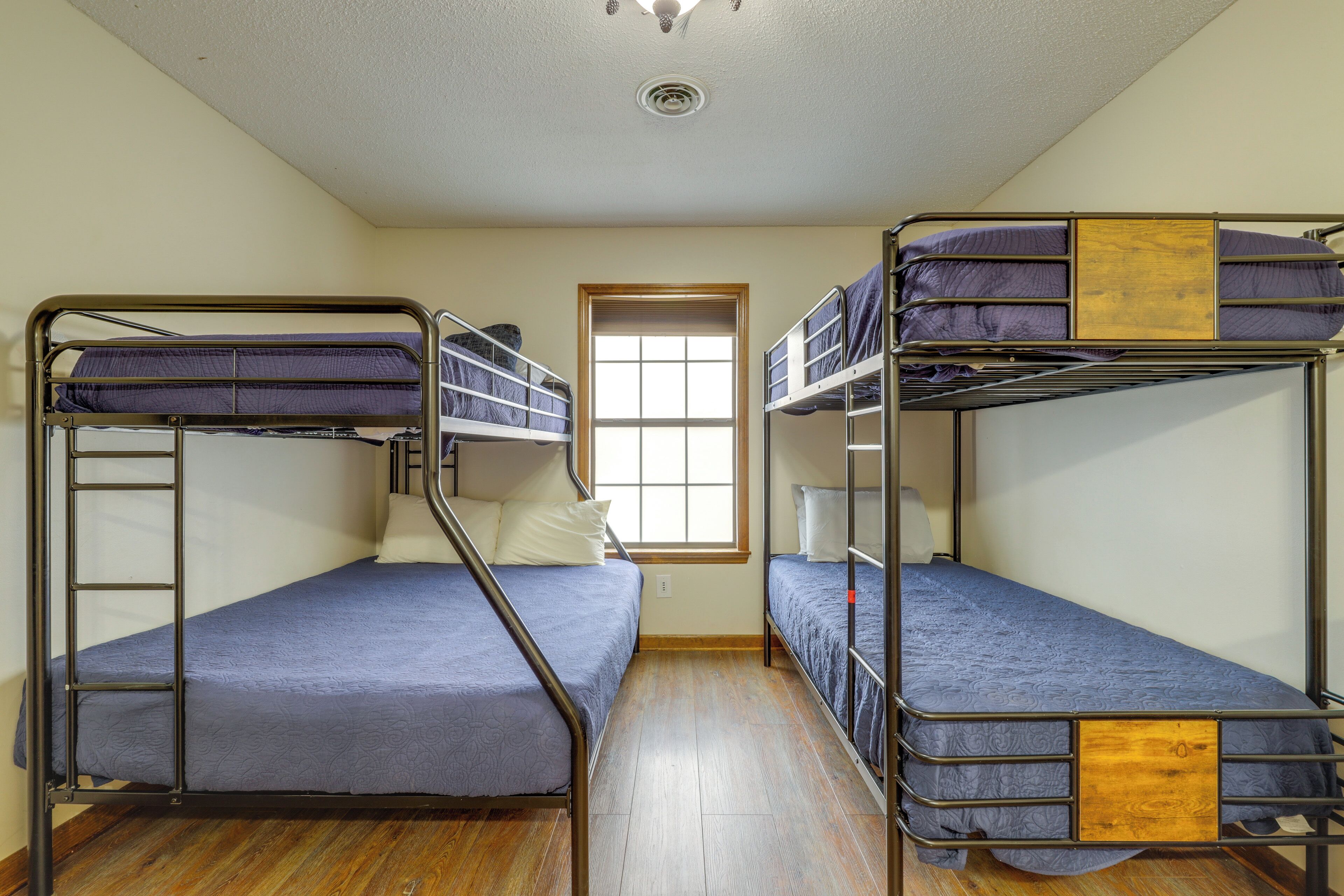A dormitory room with two bunk beds, a window, and a wooden floor.