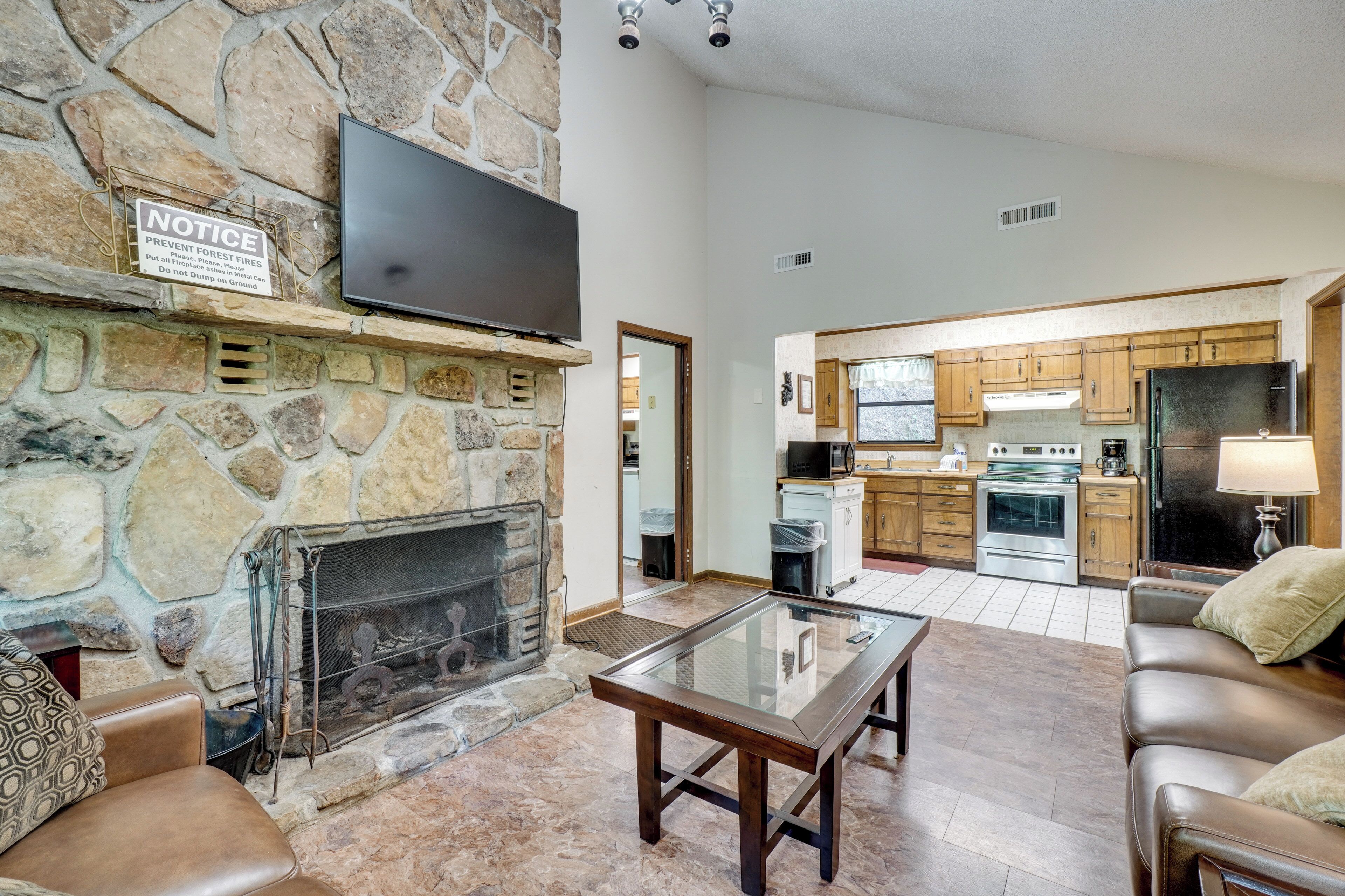 A living room with a stone fireplace, a flat-screen TV, leather sofas, and a glass coffee table.