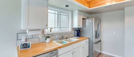 Eine moderne Küche mit weißen Schränken, einer Holz Arbeitsplatte, einem Edelstahlkühlschrank und einem integrierten Geschirrspüler.