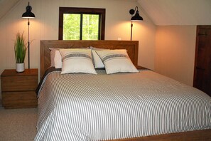 A bedroom with a wooden headboard, two bedside lamps, a striped bedspread, and a potted plant on a nightstand.
