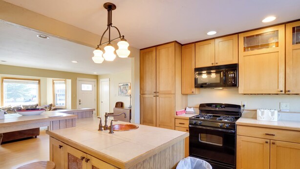 A kitchen with wooden cabinets, a central island with a sink, a stove, and a microwave. - Quaint Leadville Home w/ Grill: Walk to Dtwn! (Leadville)