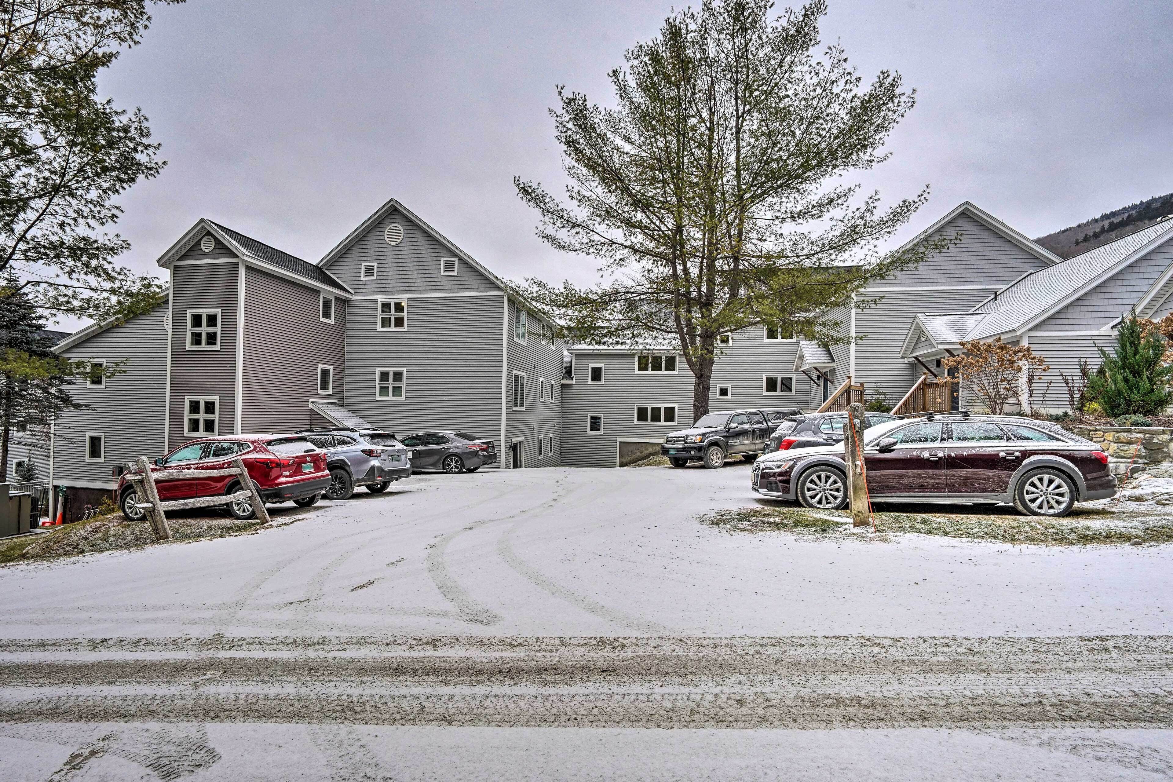 A residential area with multiple two-story houses, a snow-covered driveway, and parked cars.