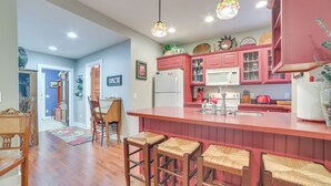Cocina con isla roja, taburetes de madera y armarios rosados.