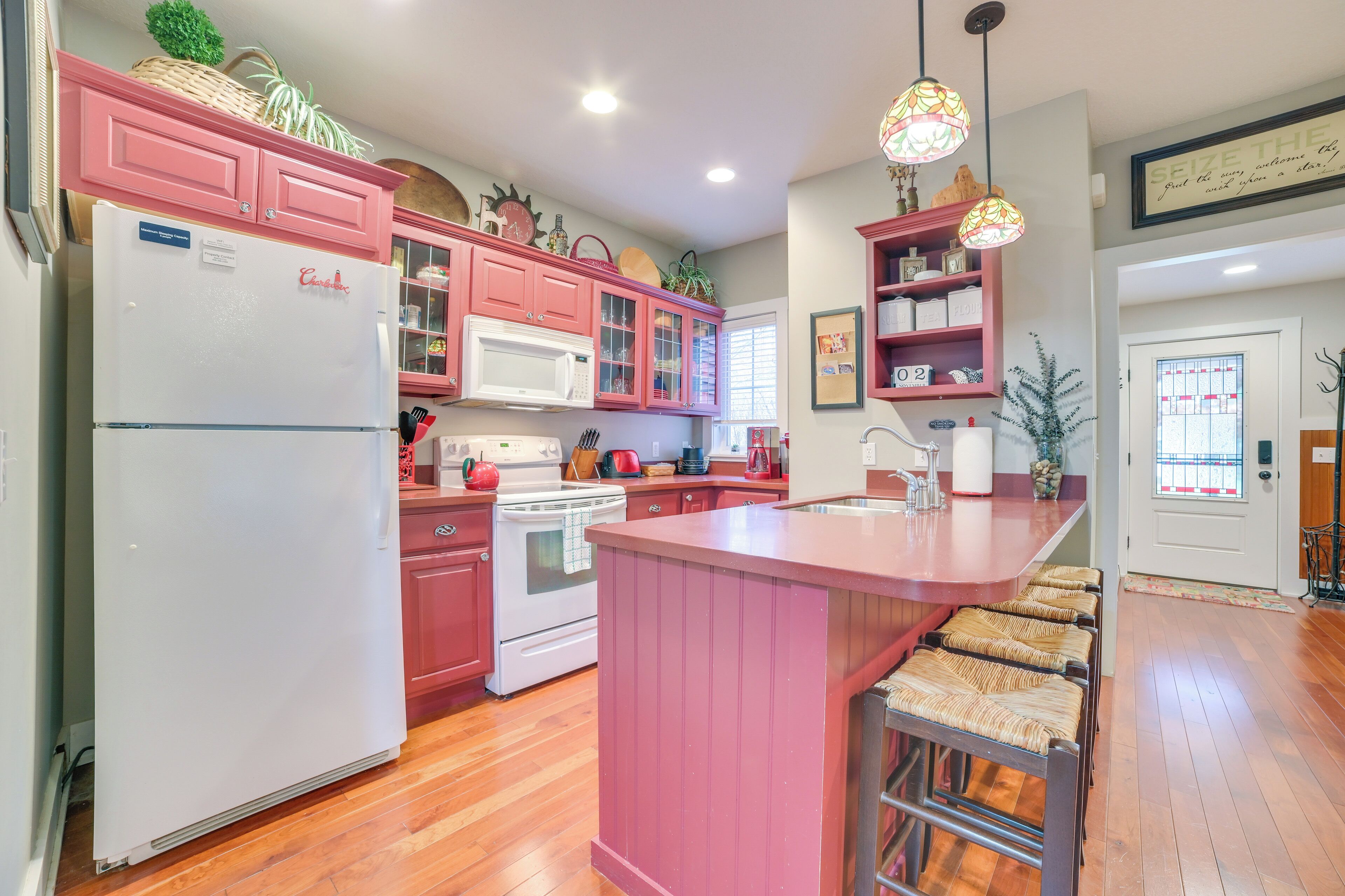 Cocina con armarios rosados, un refrigerador blanco, microondas y estufa. Cuenta con una barra y taburetes.