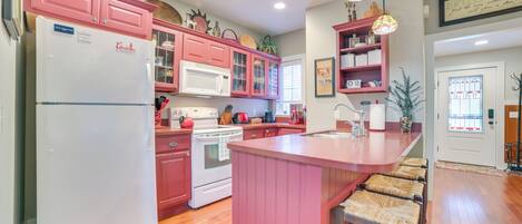 Cocina con armarios rosados, un refrigerador blanco, microondas y estufa. Cuenta con una barra y taburetes.
