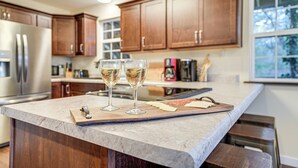 Une cuisine avec des meubles en bois, un plan de travail en marbre, un réfrigérateur en acier inoxydable et deux verres de vin.