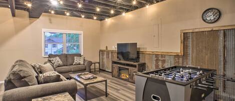 A cozy living room with a sofa, coffee table, TV, fireplace, and foosball table.