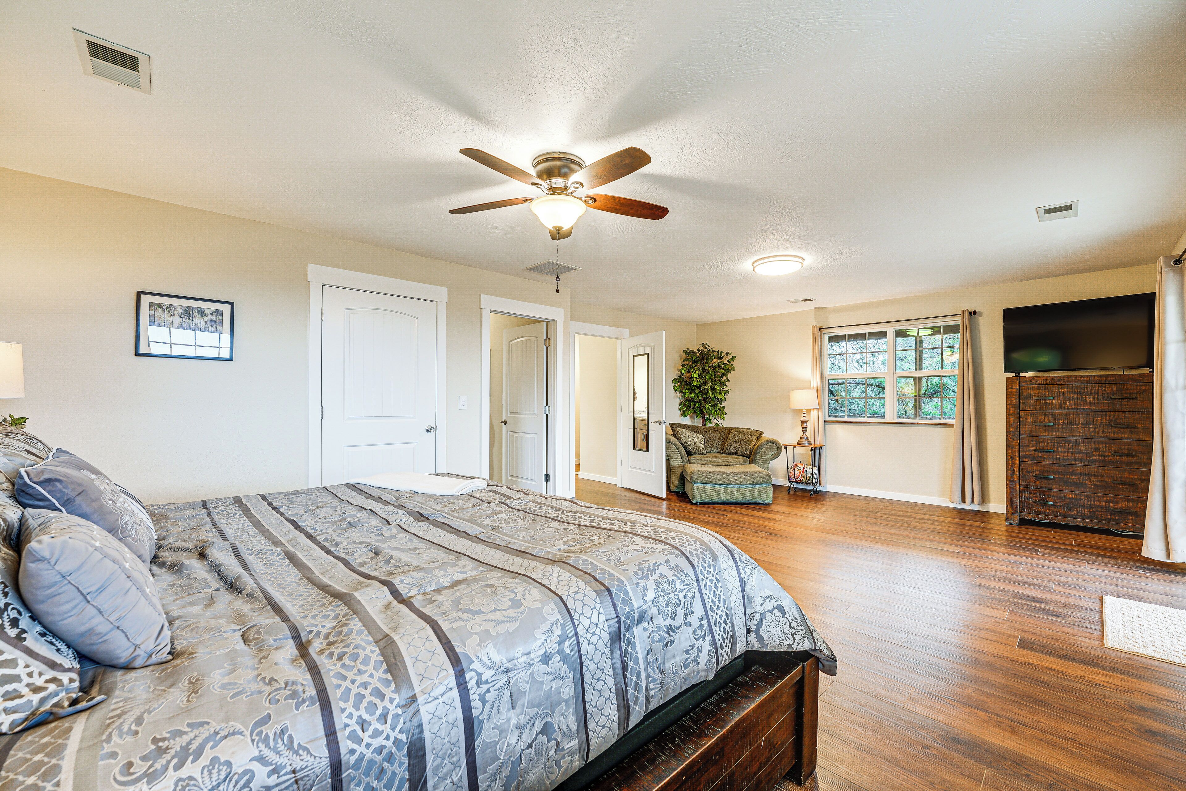 A bedroom with a large bed, a ceiling fan, a window with curtains, and a wooden dresser.