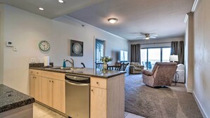 A modern kitchen with granite countertops, a dishwasher, and a dining area with a chair and table. - Sunny Beachfront Biloxi Condo w/ Resort Amenities! (Biloxi)