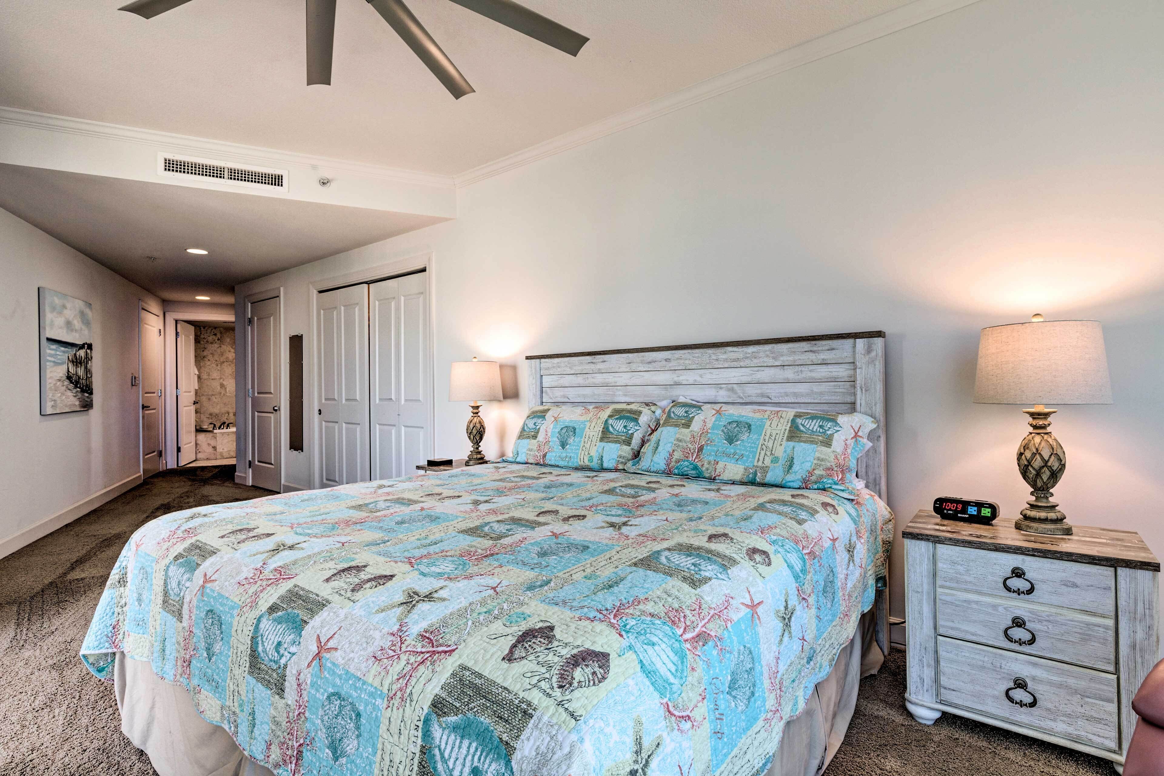 A bedroom with a bed, nightstands, and a lamp. There is a door leading to another room.