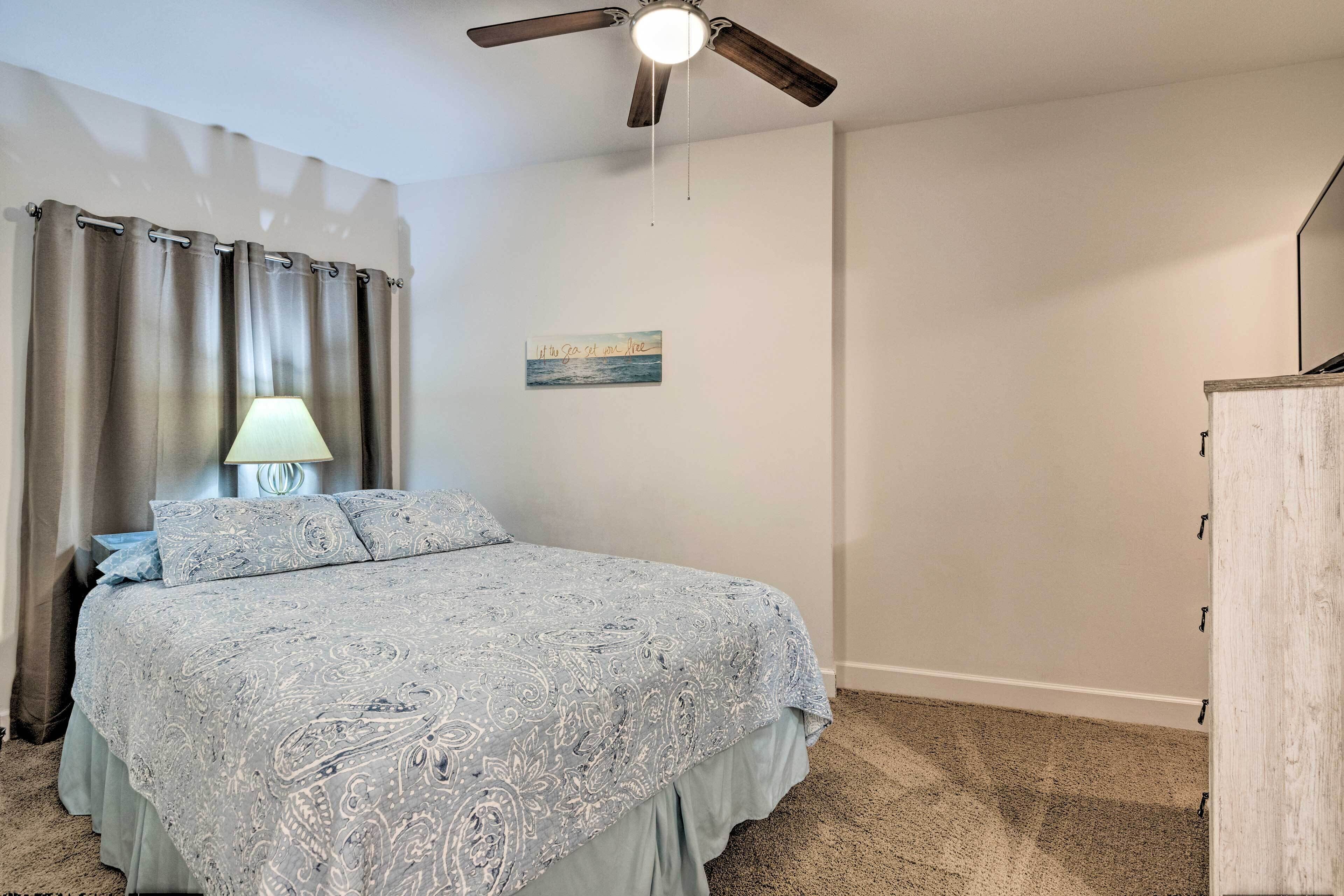 Un dormitorio con cama, ventilador de techo, lámpara, una obra de arte en la pared y un armario de madera.